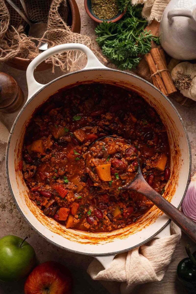 A wooden ladle resting in the pot of finished turkey apple chili.