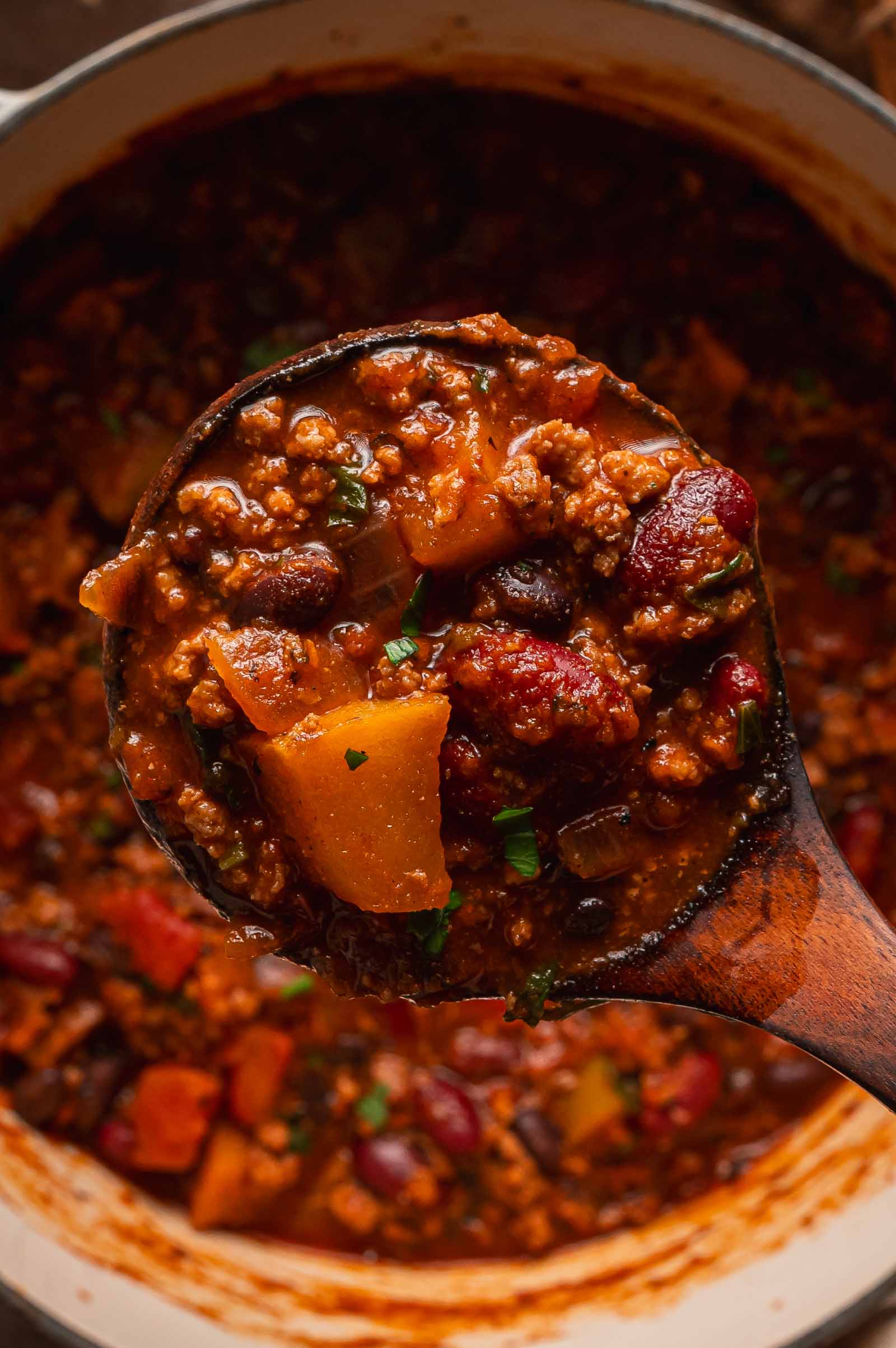 A wooden ladle holding a serving of turkey apple chili above the pot.