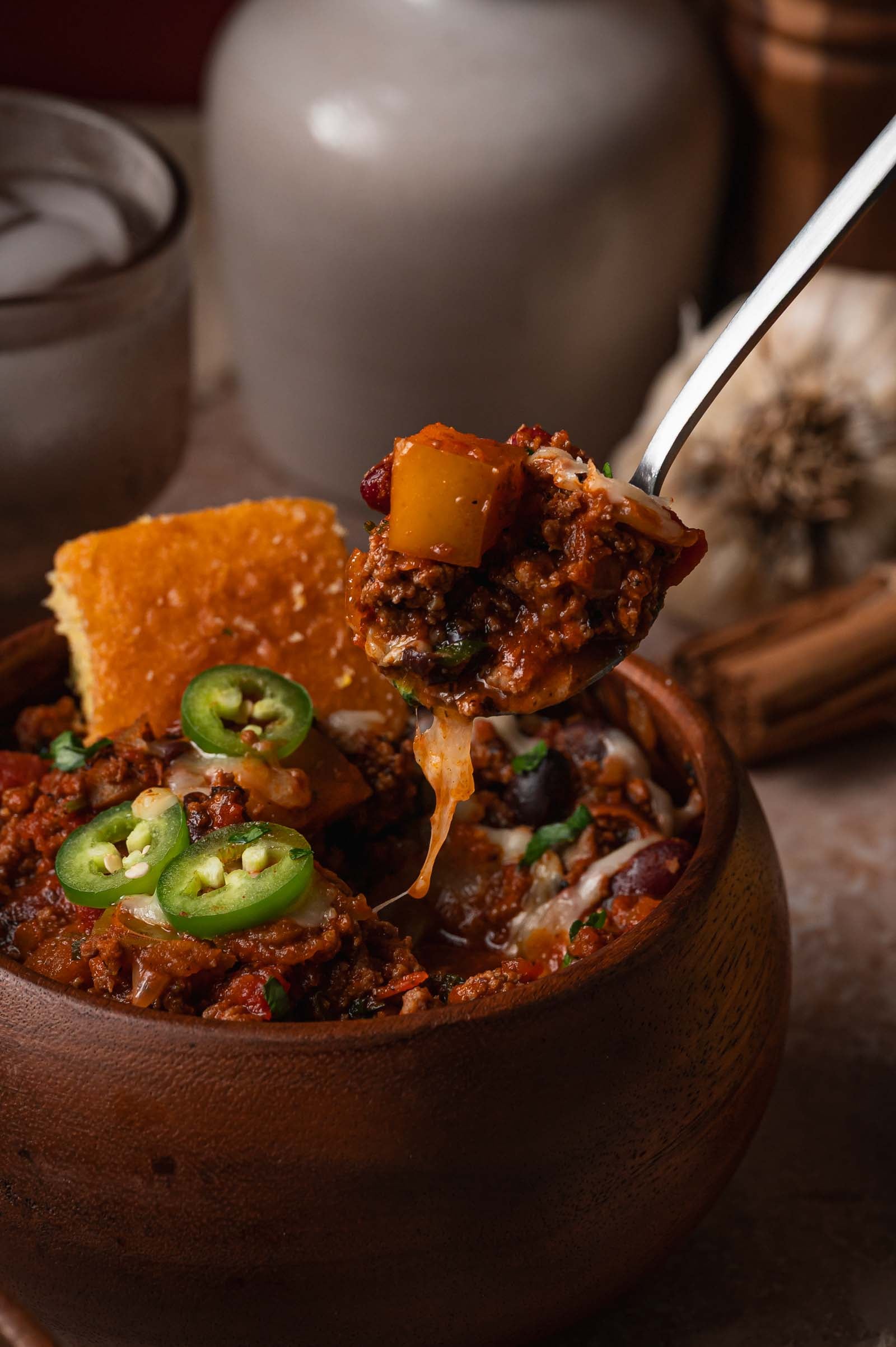 A spoonful of turkey apple chili lifted from the bowl, cheese pulling and an apple chunk on the spoon.