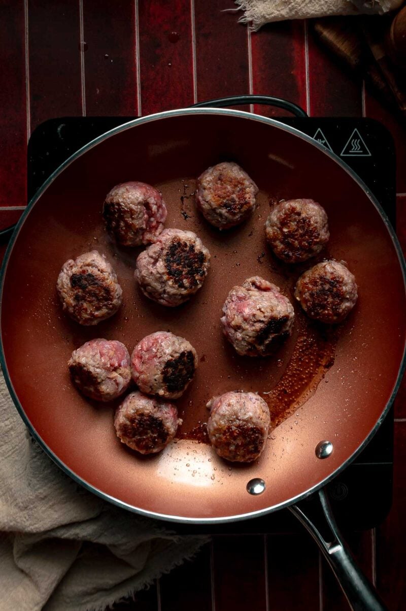 Meatballs turned in the skillet to show the dark brown crust on their seared sides.