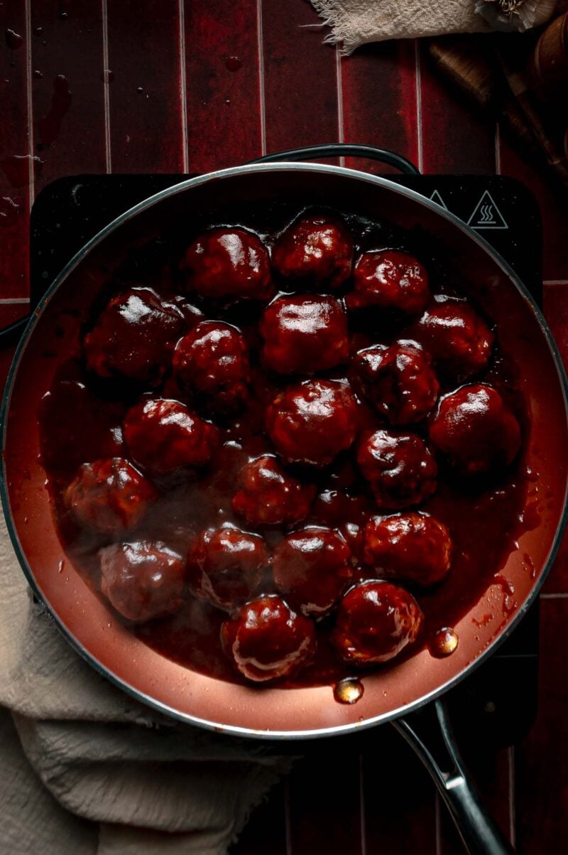 Apple butter BBQ meatballs steaming in the skillet, turned until every one is coated in thick, glossy glaze.