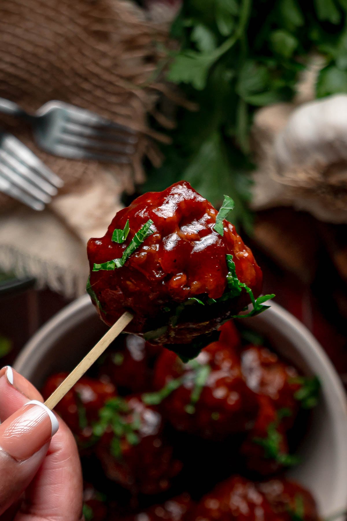 A sticky apple butter BBQ meatball held up on a bamboo pick above the serving bowl.