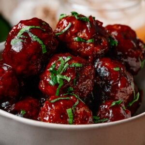 Close-up of apple butter BBQ meatballs coated in glossy glaze and chopped parsley.