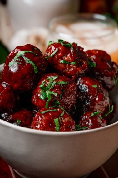 Close-up of apple butter BBQ meatballs coated in glossy glaze and chopped parsley.