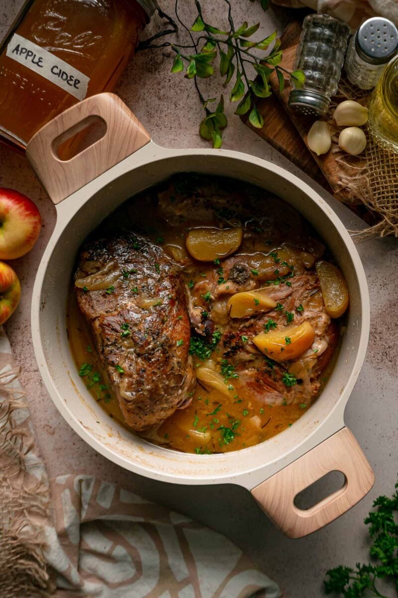 Apple cider braised pork in the Dutch oven after the sauce is thickened, with tender apple wedges and chopped fresh herbs.