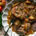 Braised pork shoulder with apple slices in a scalloped bowl.