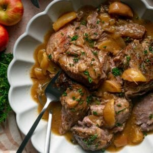 Braised pork shoulder with apple slices in a scalloped bowl.