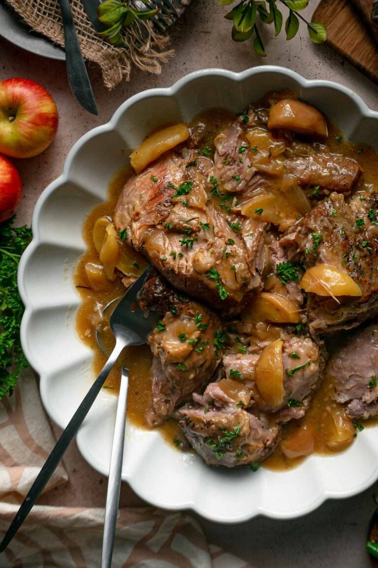 Braised pork shoulder with apple slices in a scalloped bowl.