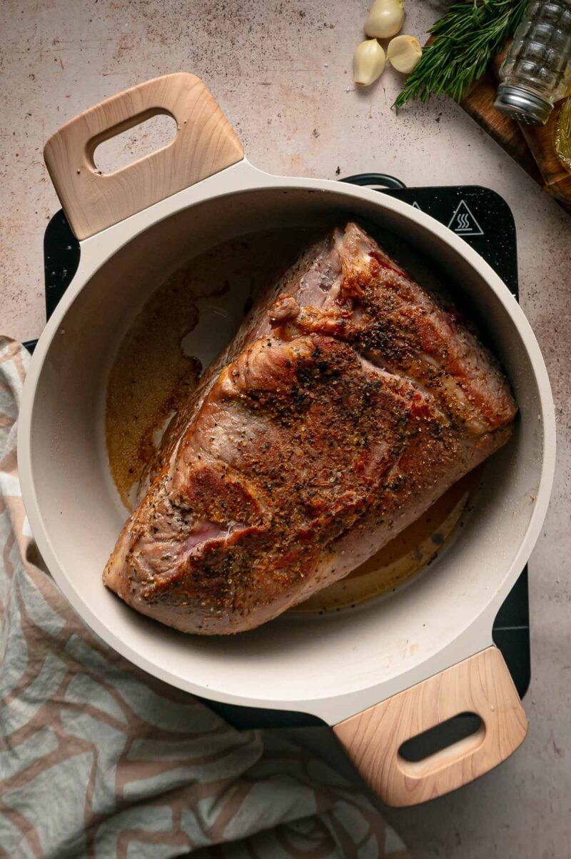 The seasoned pork shoulder searing in a Dutch oven on the stovetop until a deep brown crust forms.