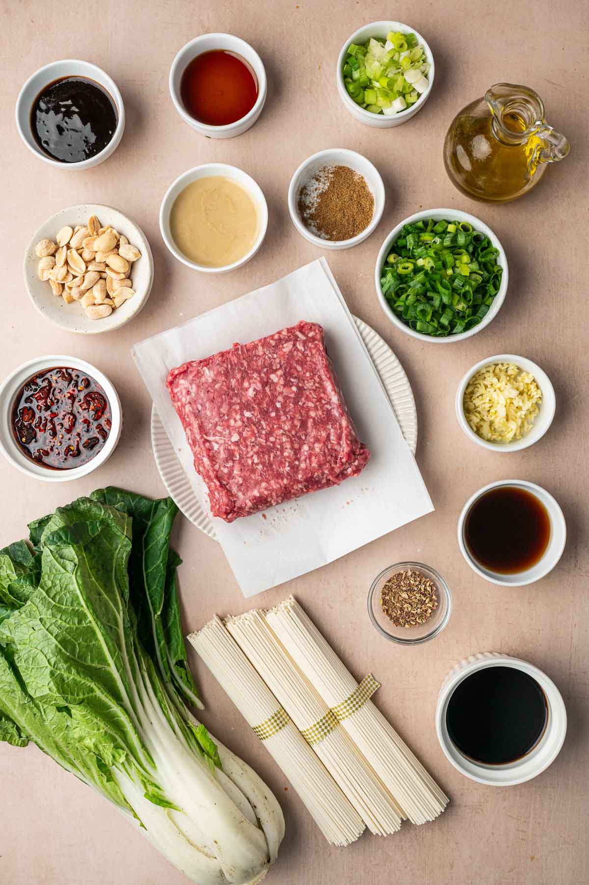 Ingredients for ground lamb dan dan noodles: a block of ground lamb, dried white noodles, bok choy, sesame paste, chili oil, peanuts, green onions and garlic.