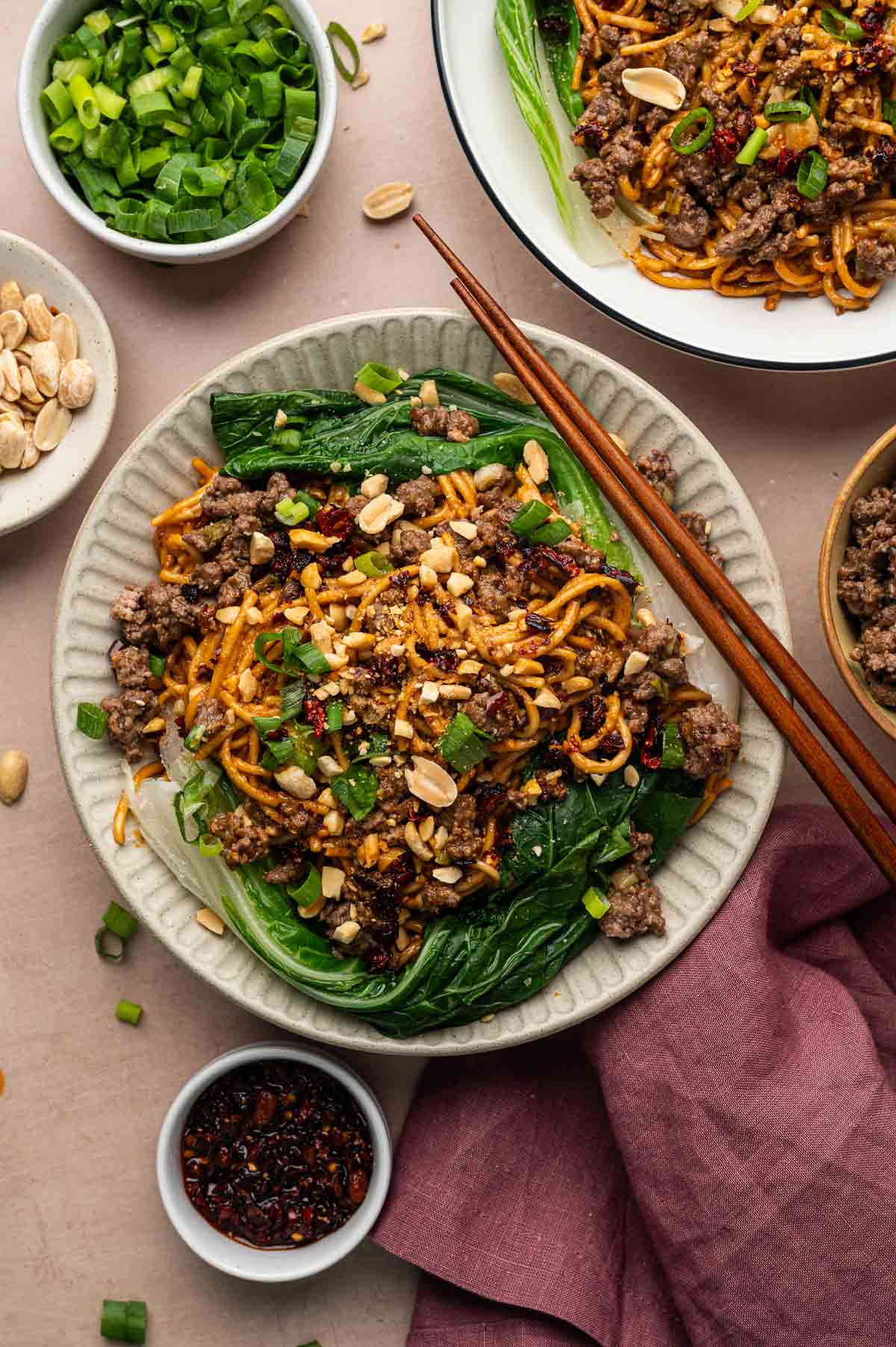 Ground lamb dan dan noodles over bok choy, topped with peanuts and green onions, with chopsticks, chili oil and extra lamb on the side.