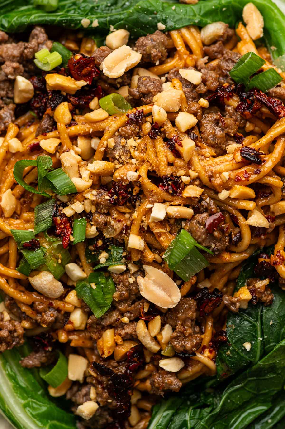 Sesame-chili noodles with ground lamb, peanuts and green onions piled on dark green bok choy leaves.