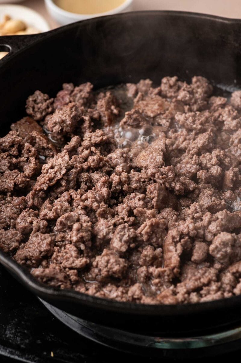 Ground lamb browning into small crumbles in a cast iron skillet.