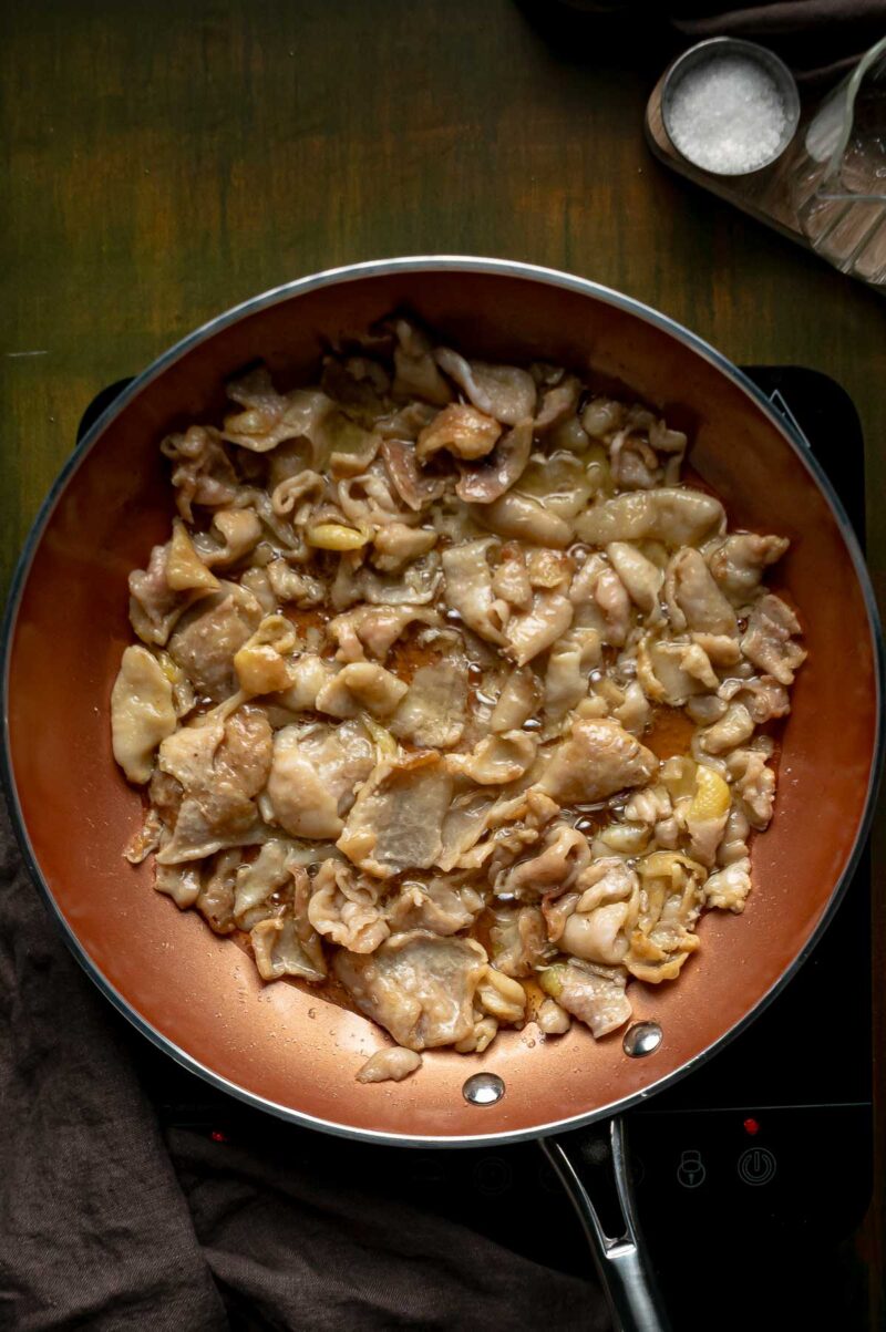 Chicken skins shrinking and turning pale golden in the skillet as the first schmaltz pools underneath.