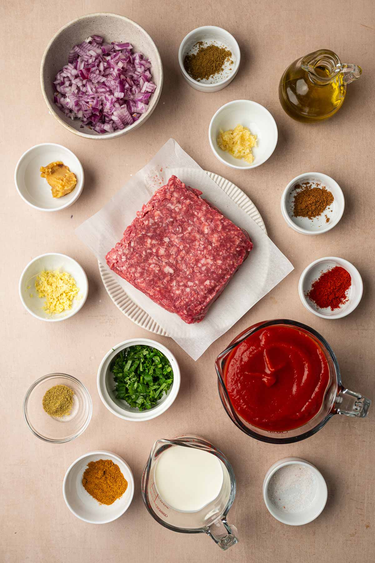 Ingredients for lamb meatball curry: ground lamb, red onion, garlic, ginger, cilantro, spices, tomato puree, heavy cream, oil and salt.