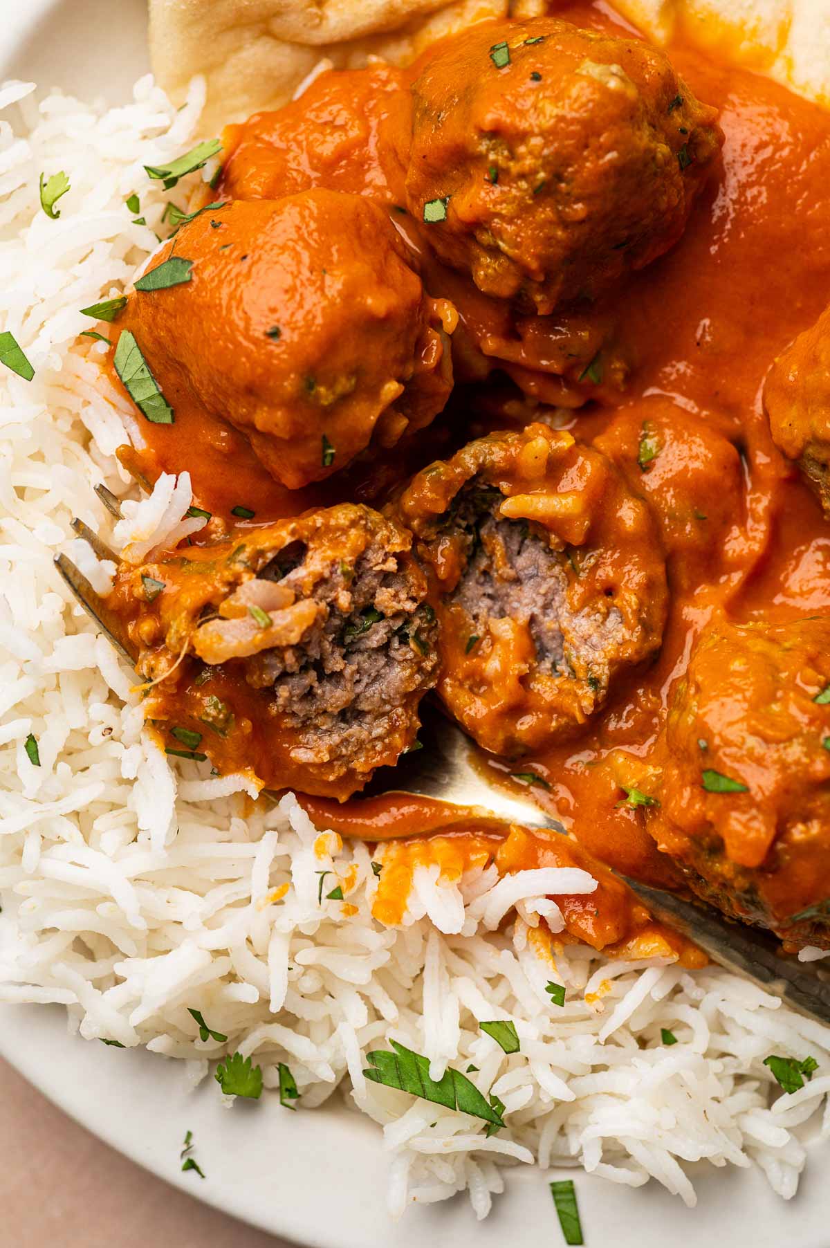 A lamb meatball split open with a fork over basmati rice, showing the cooked ground lamb inside the creamy curry sauce.