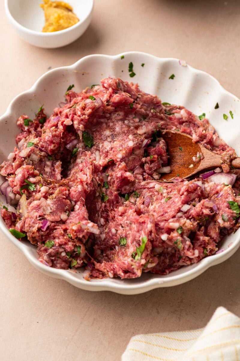 The ground lamb meatball mixture stirred together with a wooden spoon, red onion and cilantro flecked throughout.