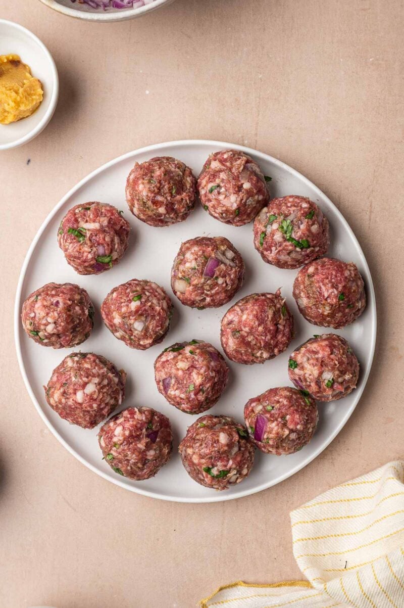 Raw lamb meatballs rolled and lined up on a white plate, ready to brown.