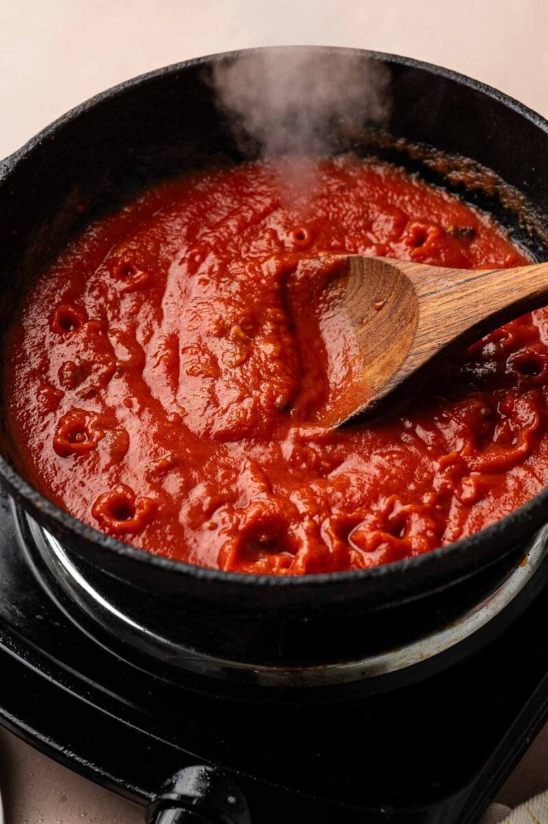 Tomato curry sauce simmering and steaming in the cast iron skillet, stirred with a wooden spoon.