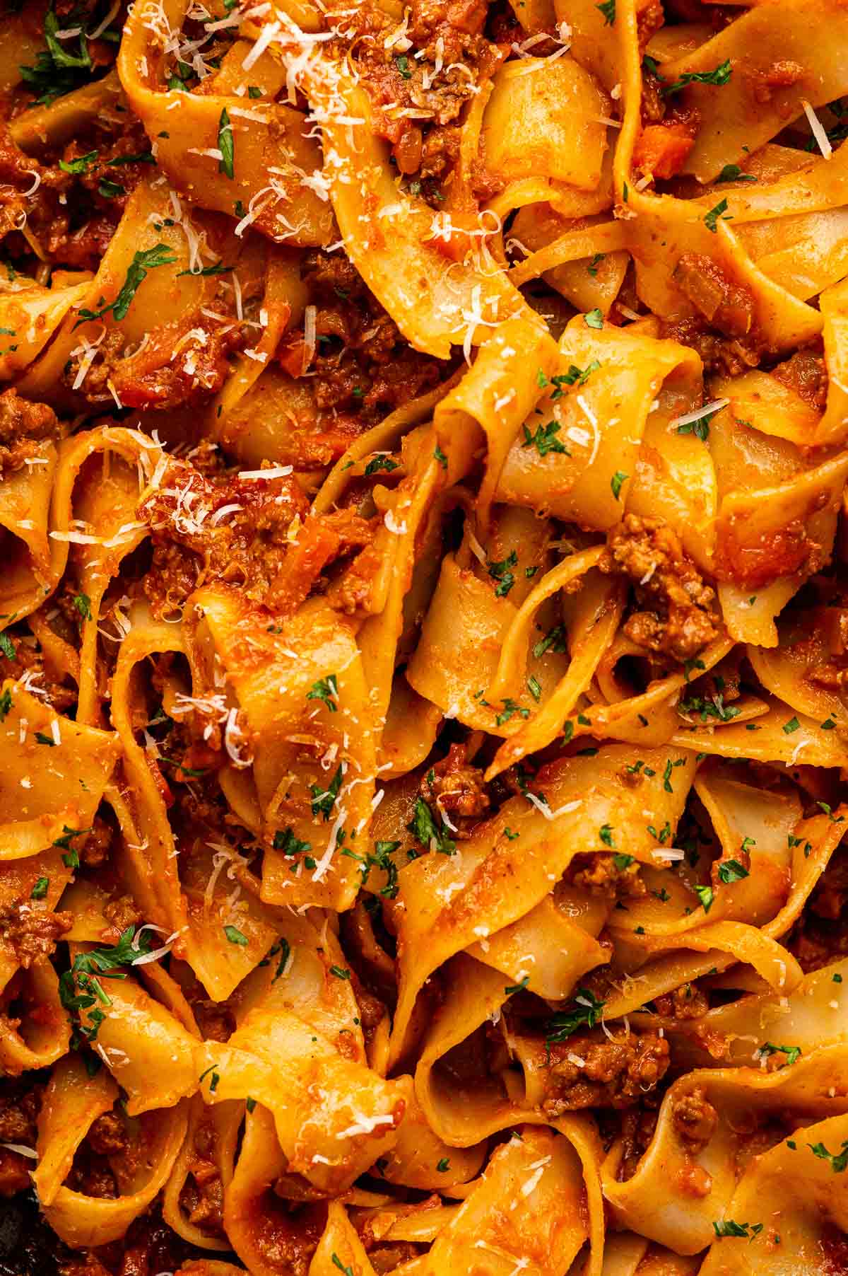Overhead close up of pappardelle and ground lamb bolognese dusted with grated Parmesan and chopped parsley.