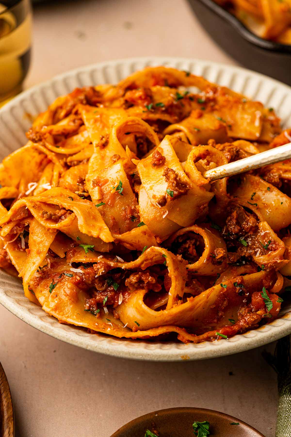 A fork twirling into a bowl of pappardelle tossed in lamb bolognese with Parmesan and parsley.