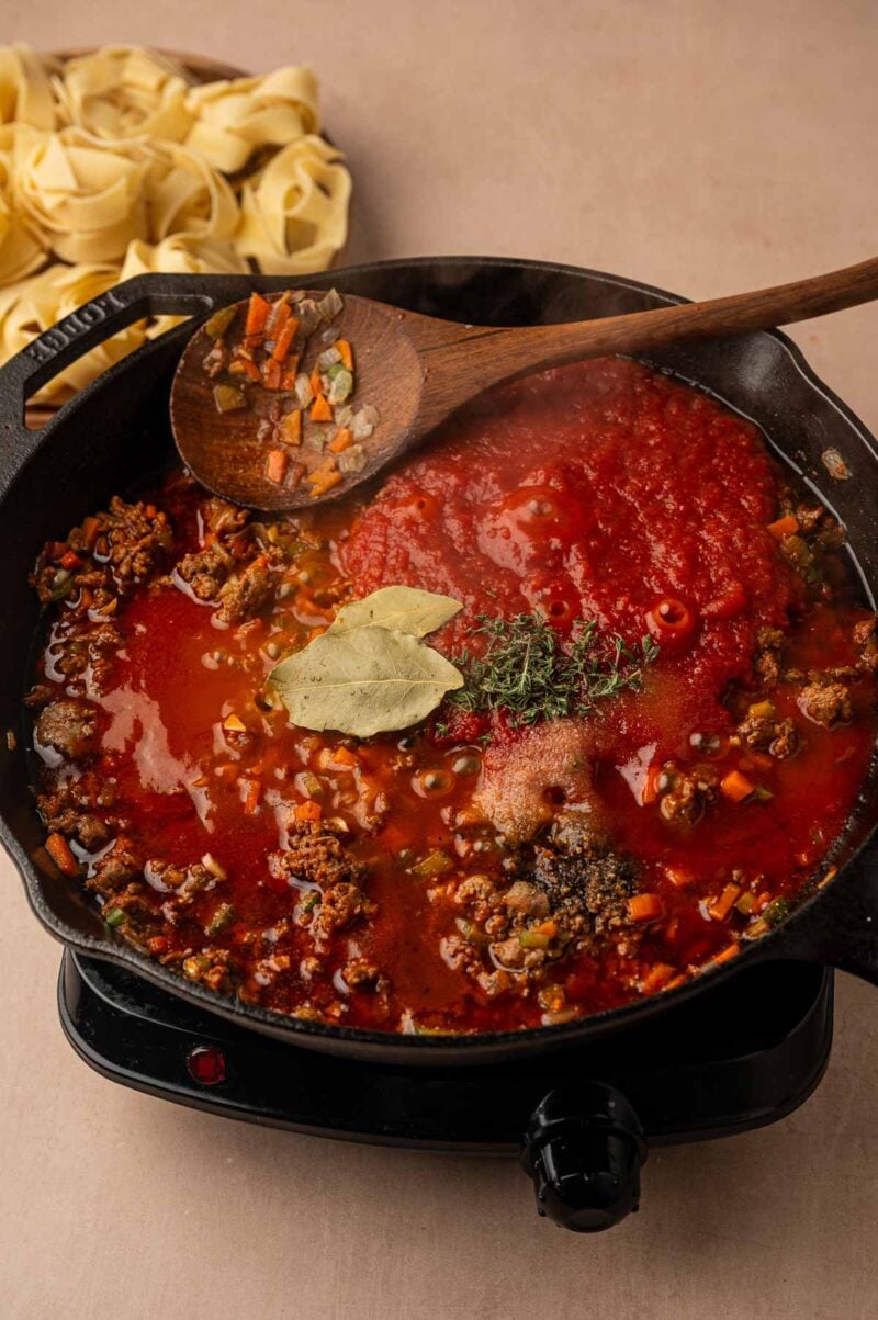 Crushed tomatoes, bay leaves, fresh thyme, salt and pepper added on top of the browned lamb and vegetables in the skillet.