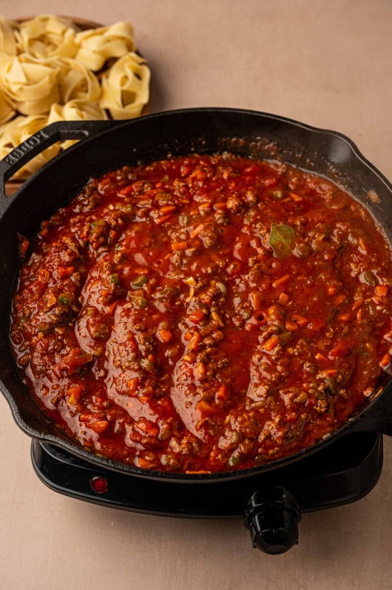 The lamb bolognese sauce just stirred together in the cast iron skillet, with pappardelle nests waiting behind it.