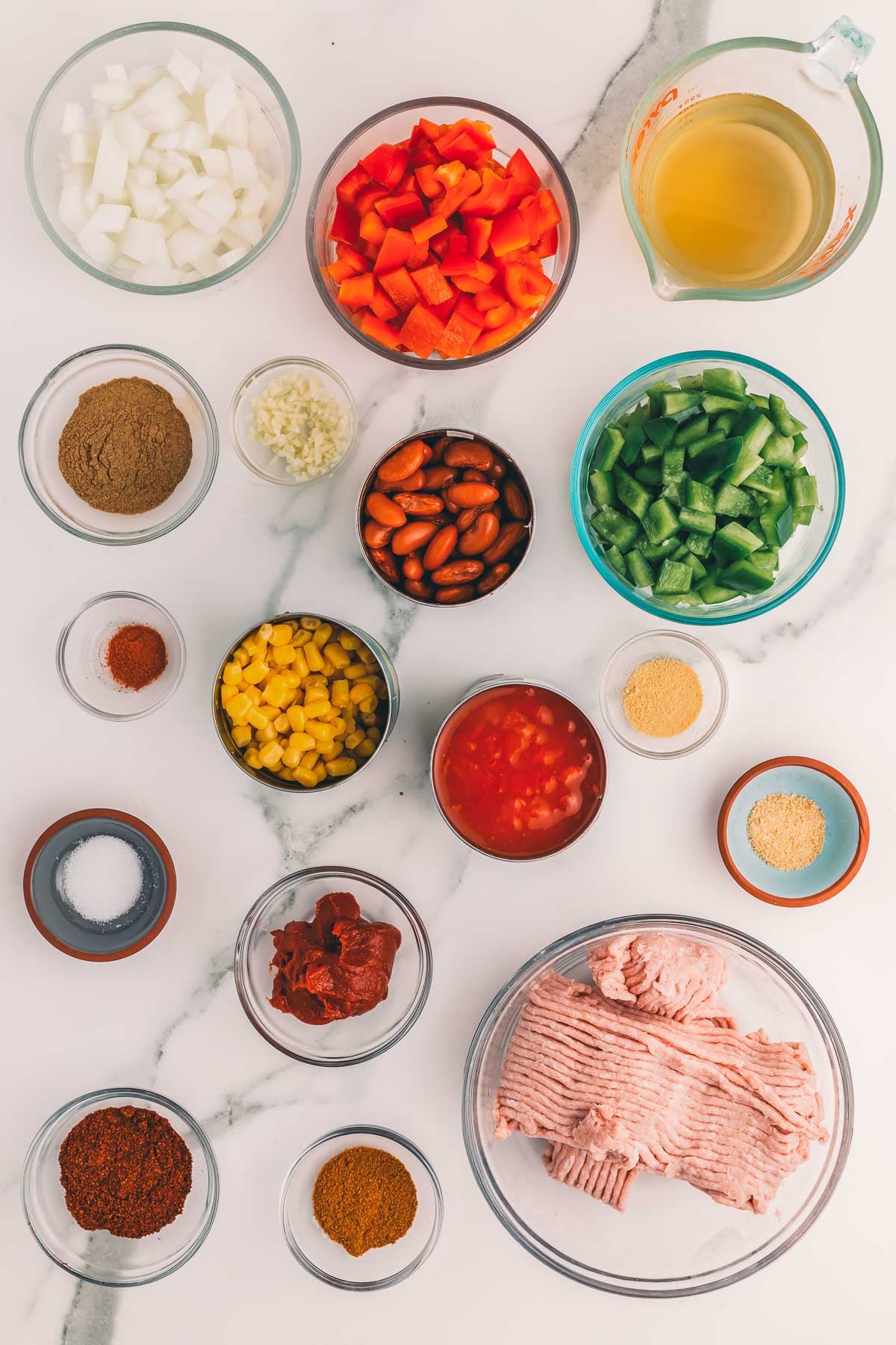 Ingredients for slow cooker turkey chili: raw ground turkey, diced onion, red and green bell peppers, kidney beans, corn, diced tomatoes, tomato paste, chicken broth and spices.
