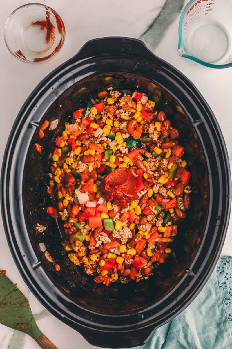 A dollop of tomato paste on top of the stirred turkey chili mixture in the slow cooker, ready to cook.