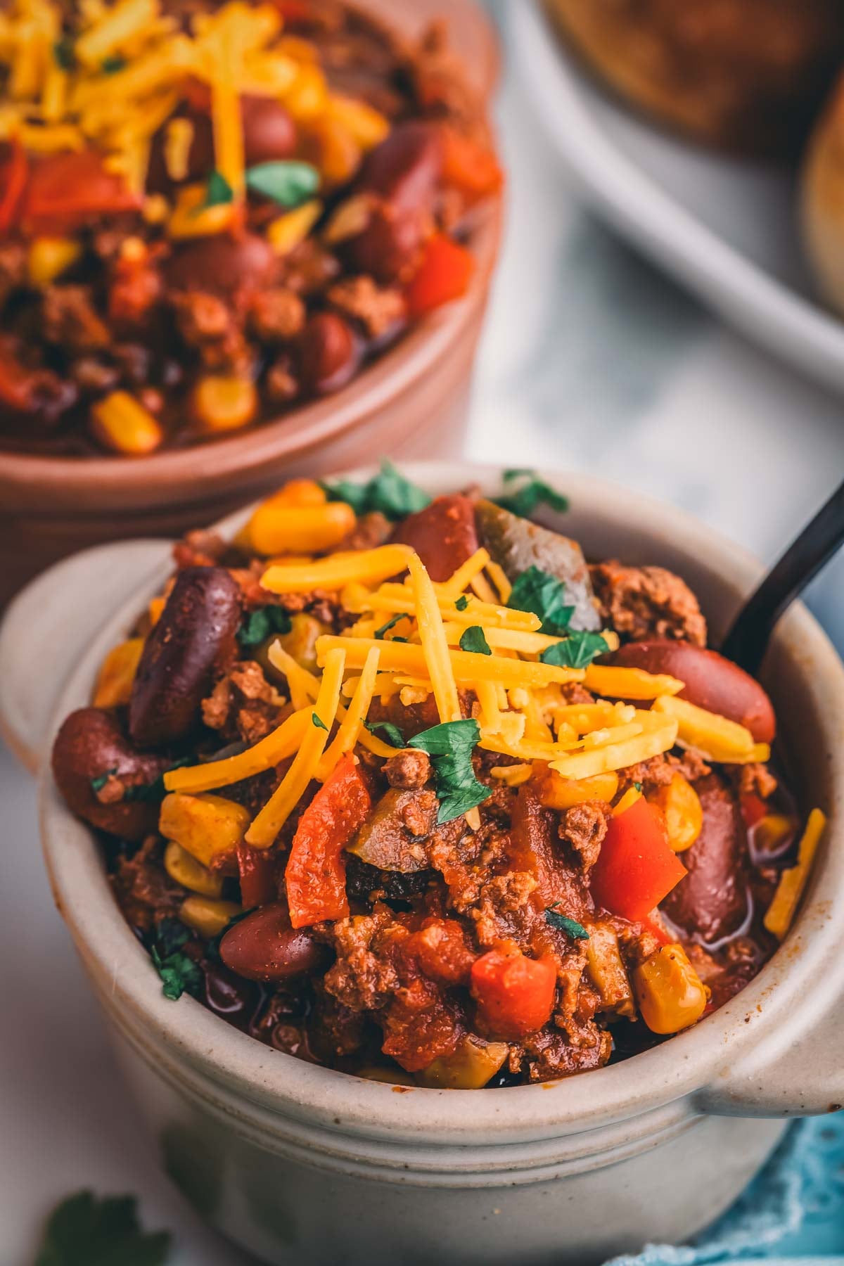 Close up of turkey chili loaded with kidney beans, corn and red peppers under shredded cheddar and fresh herbs.