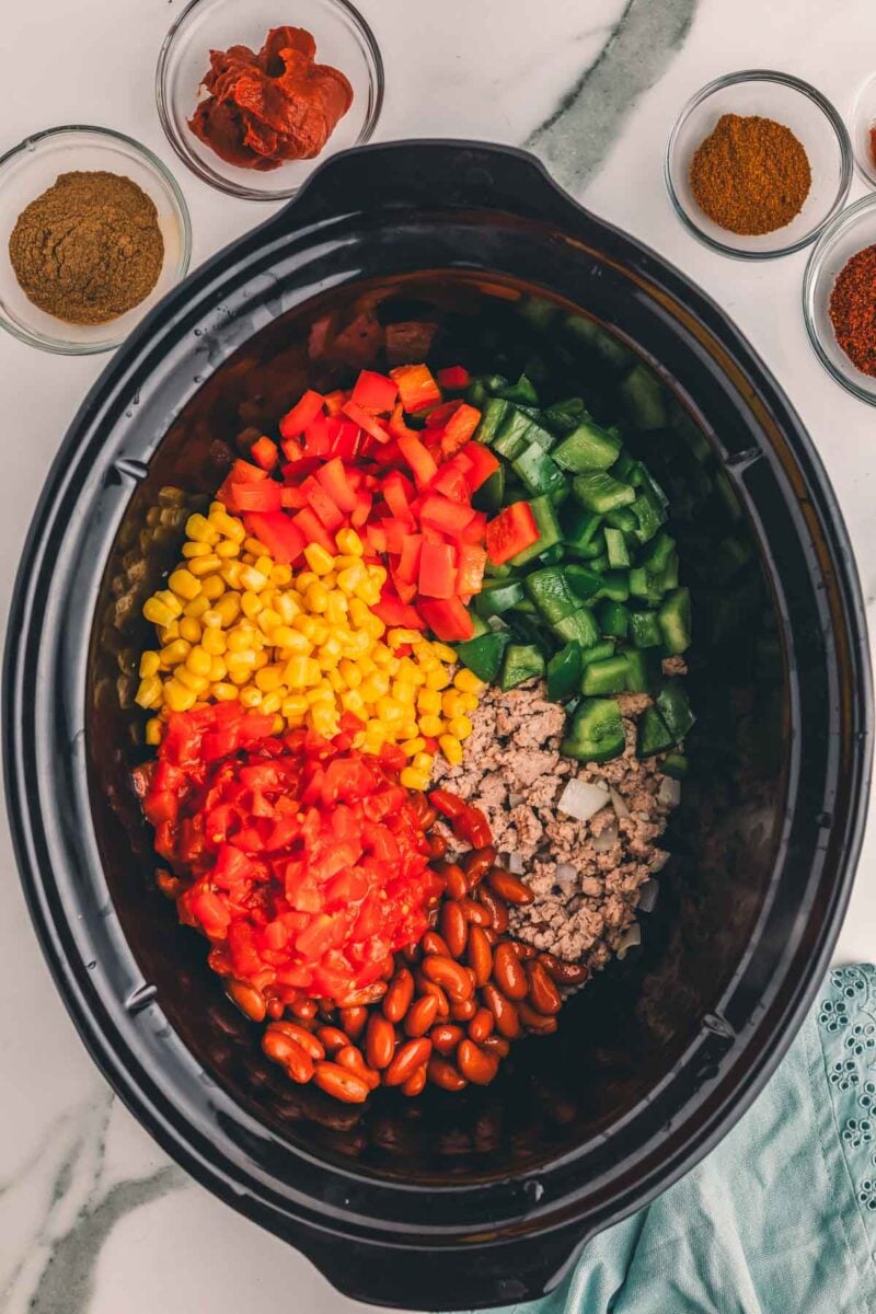 Red and green bell peppers, corn, diced tomatoes and kidney beans layered over the ground turkey in the slow cooker.